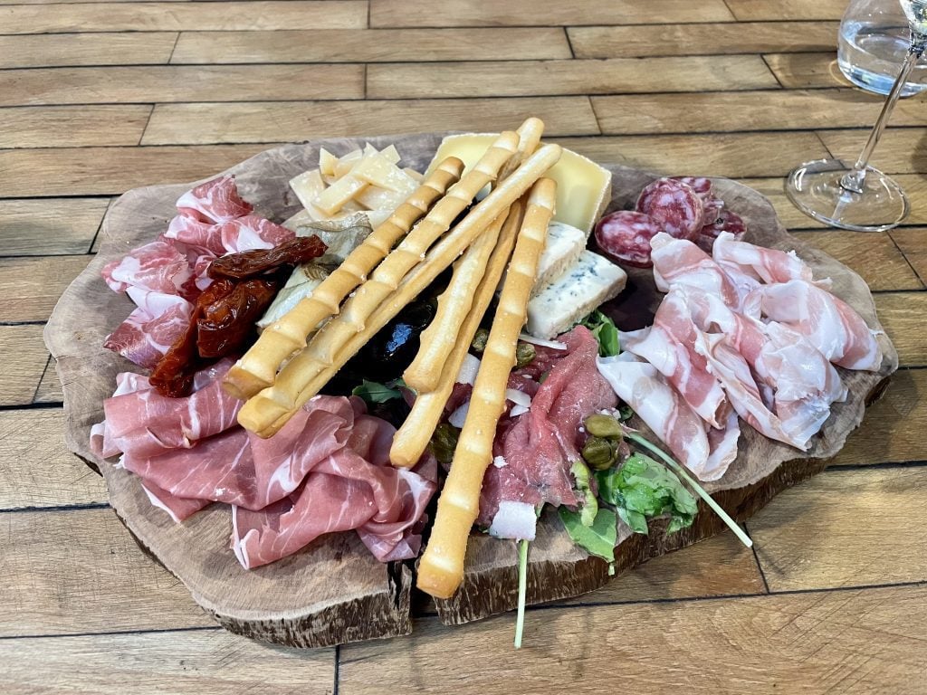 A plate of Italian salume -- sliced cured meats, cheeses, and breadsticks.