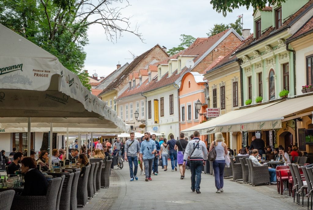 People walking down a cobblestoned street with colorful buildings and street cafes.