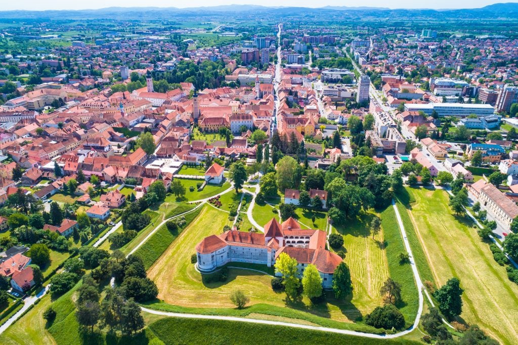 An aerial shot of a pretty-looking small town with orange roofs and a white and orange castle.