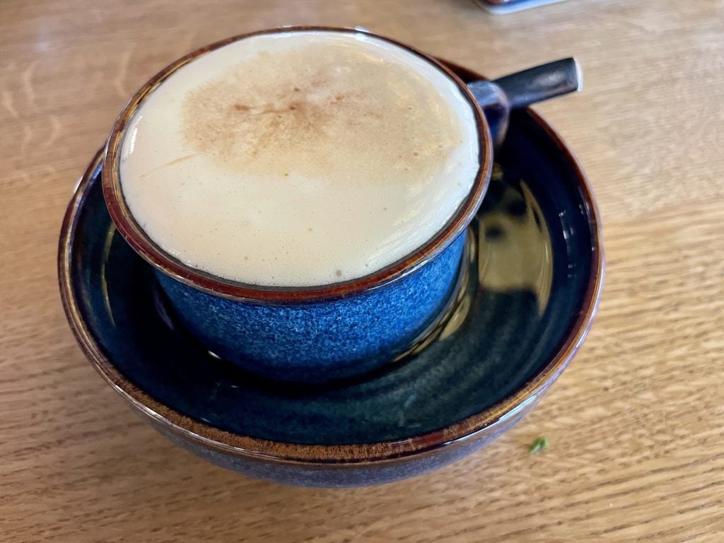 A marshmallowy looking coffee in a ceramic cup and saucer.