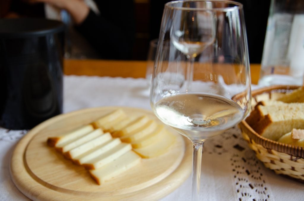 A glass of white wine in front of a plate of two different cheeses.