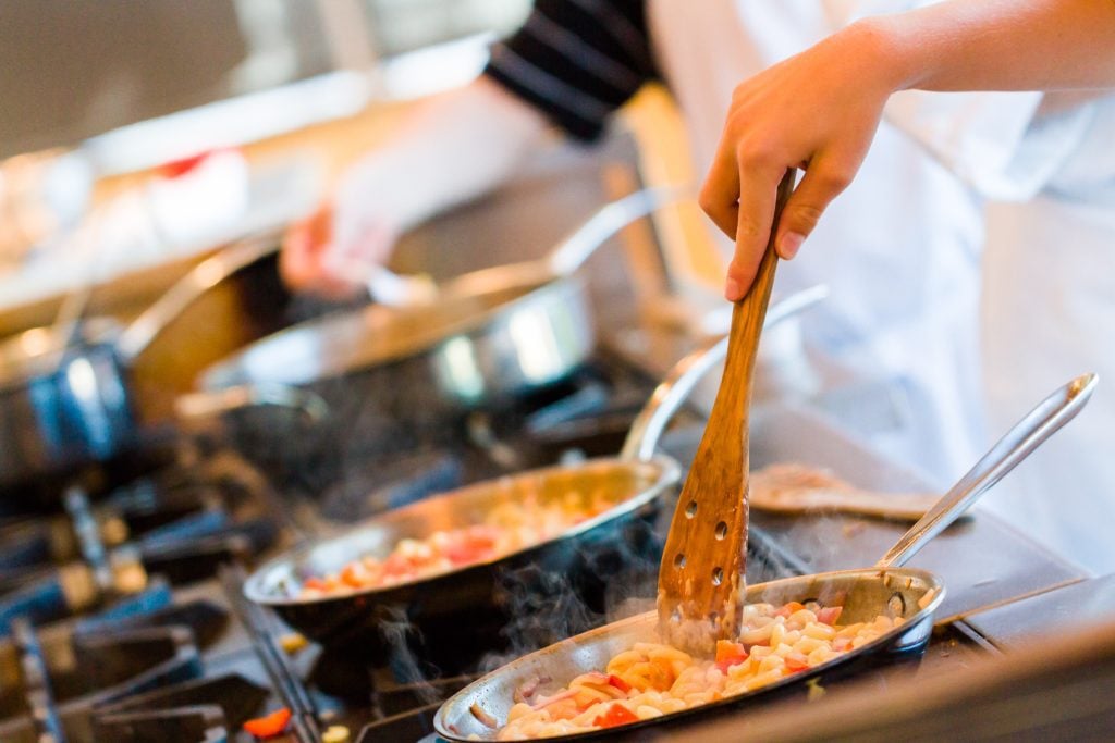 People cooking in a kitchen over bubbling pots.