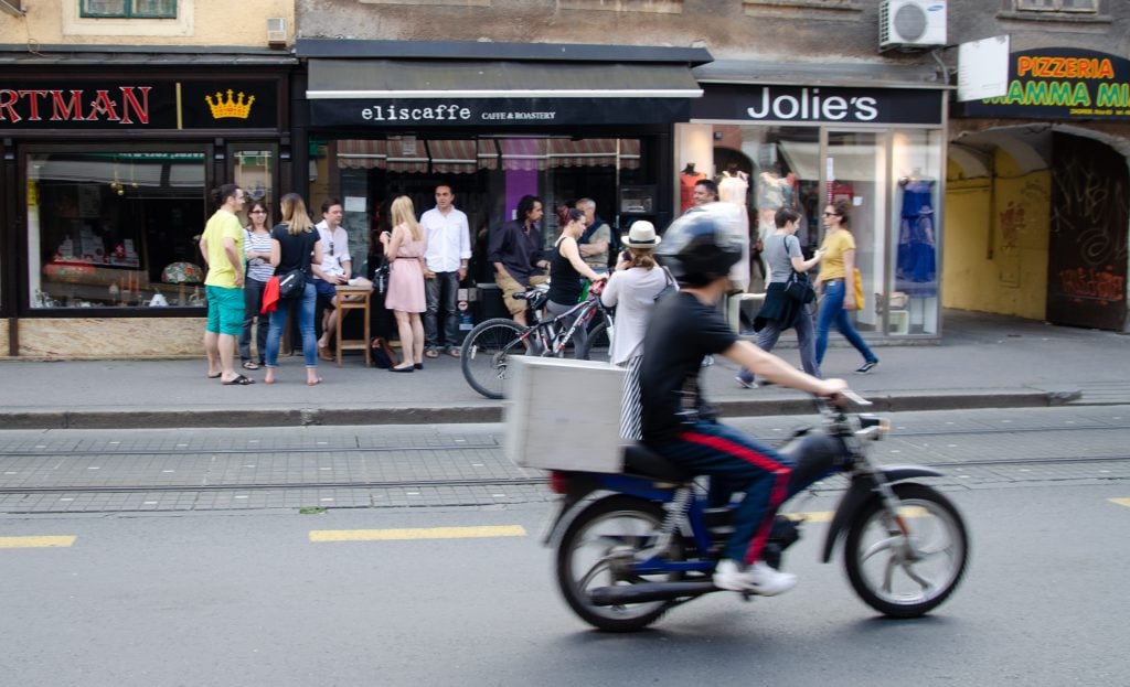 A cyclist in Zagreb riding past a busy coffee shop.