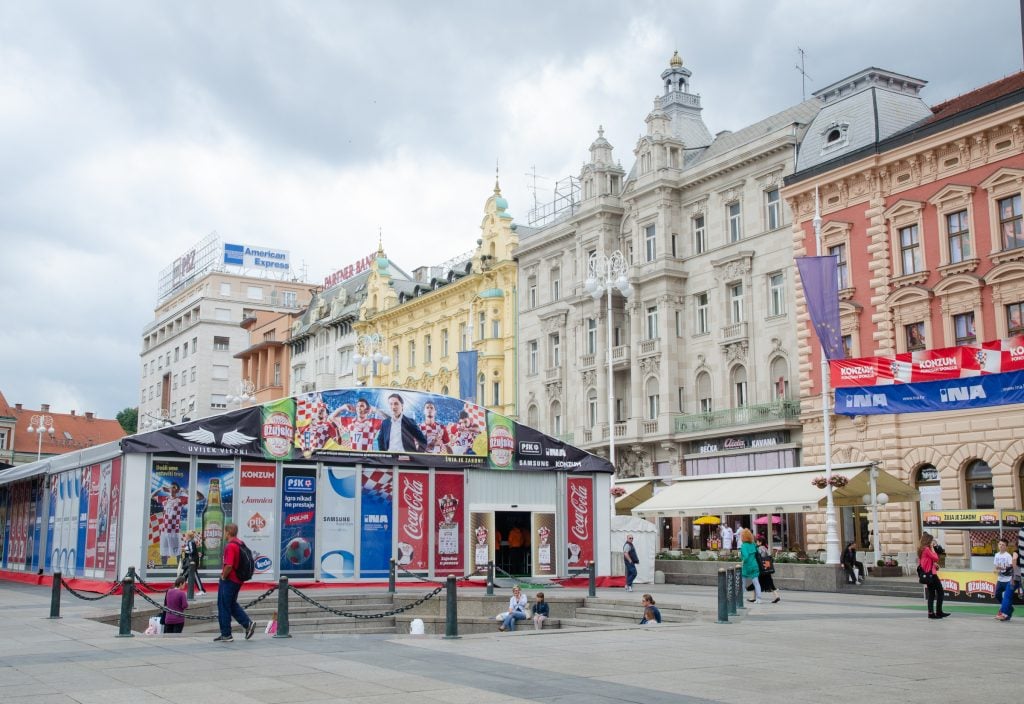 A row of crenellated buildings in Zagreb and a building celebrating the World Cup in front of it.