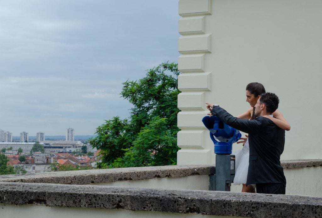 A couple with their arms around each other, peering into a telescope overlooking Zagreb.