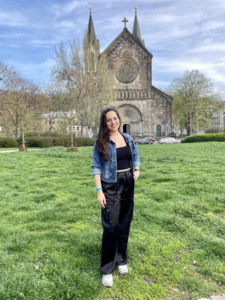 Kate wearing black satin cargo pants, a black top and a denim jacket, in front of a church.