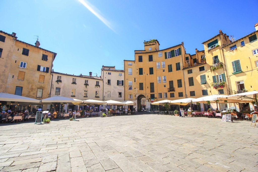 A view of a square in Lucca, Italy with vendors selling under tents and yellow buildings in the background