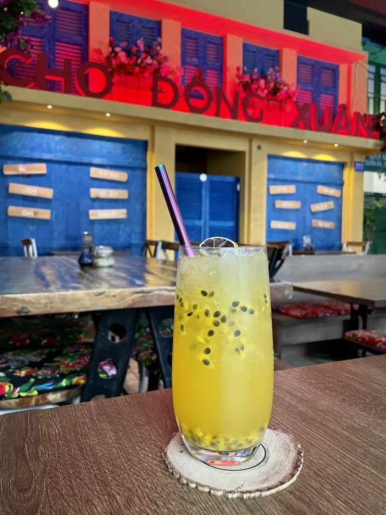 A glass of bright yellow lemonade filled with passionfruit seeds at a Vietnamese restaurant.