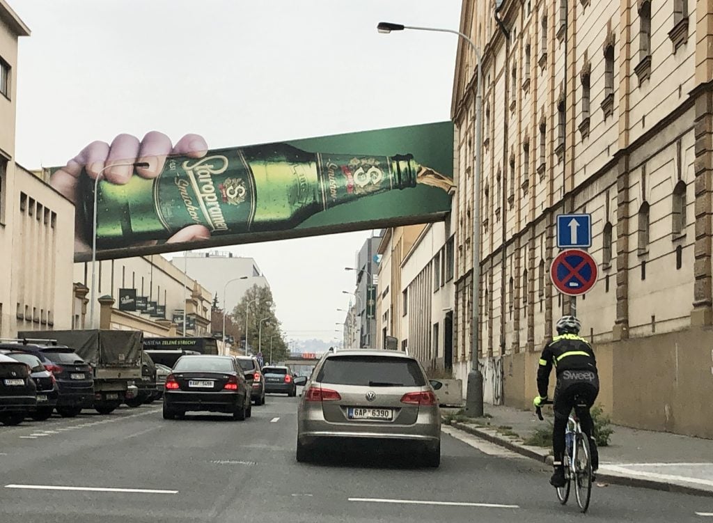 A giant billboard above a street, looking like a person drinking an enormous Staropramen beer.