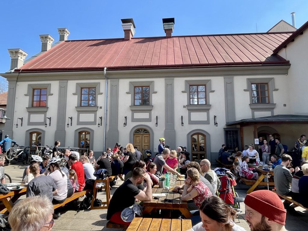 Crowds of people sitting at an outdoor beer garden, drinking beer in the sunshine.