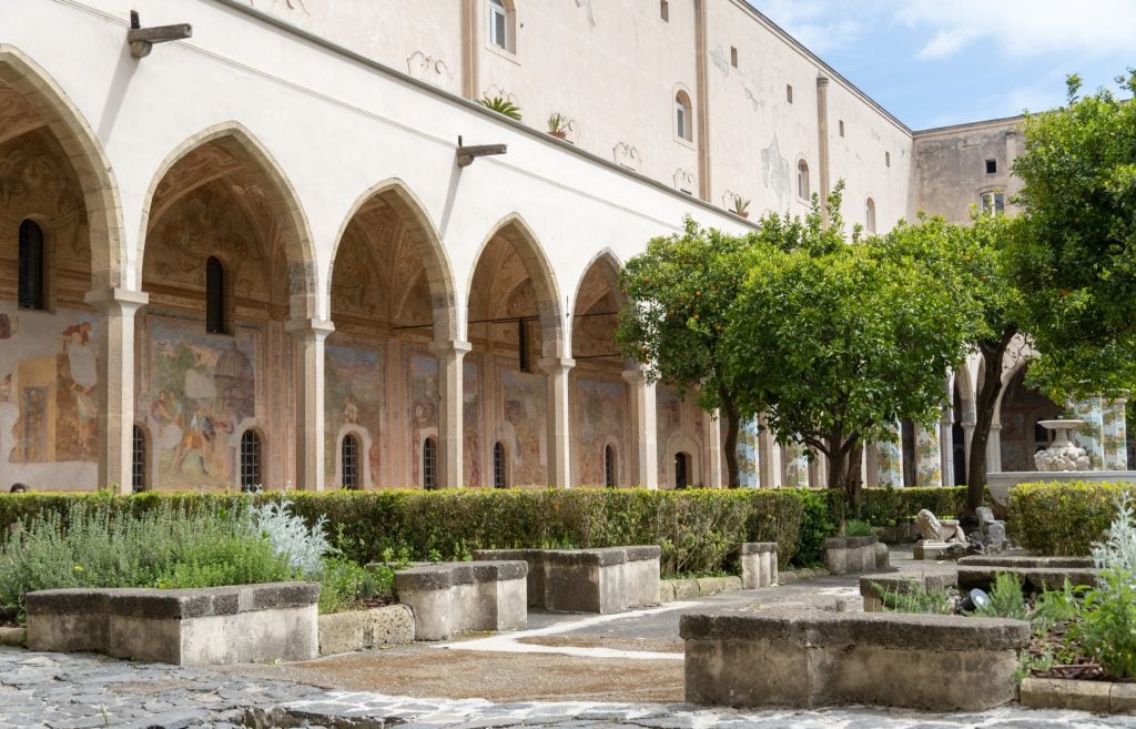 A courtyard in Naples filled with plants, surrounded by stone columns.