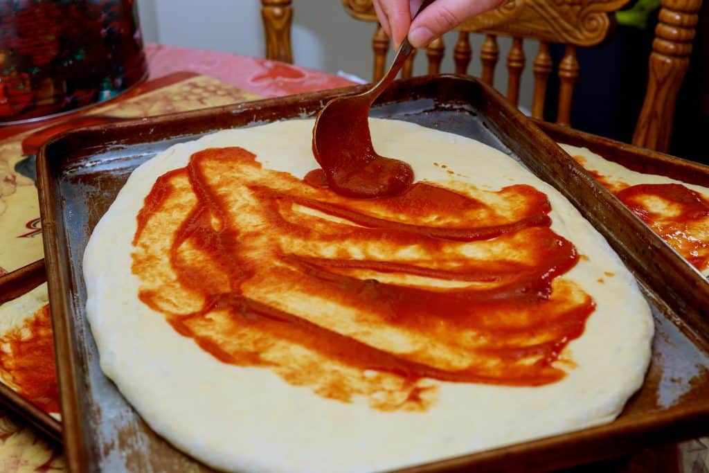 Pizza dough being covered with tomato sauce.