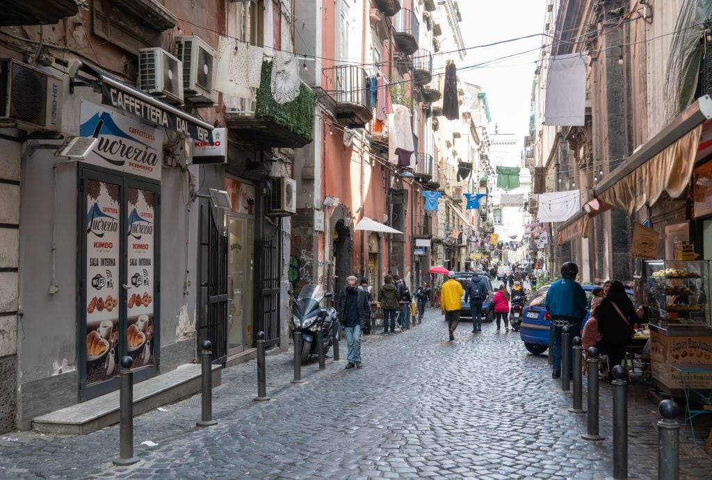 A crowded cobblestone street in Naples, laundry strewn between two windows.