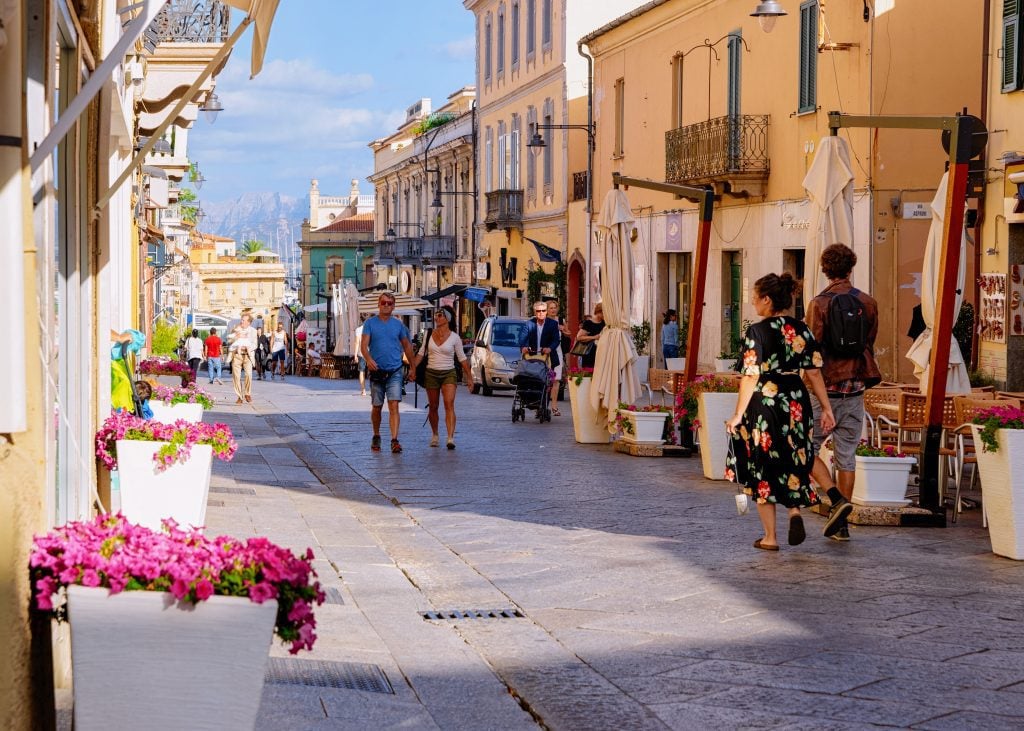 People walking down a pedestrian-only street leading to a marina in Olbia, Sardinia.