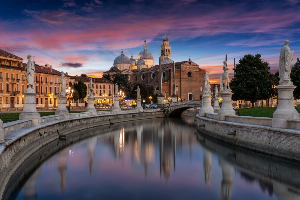 A pink and purple sunset over a moat in Padova, Italy, a church in the background.