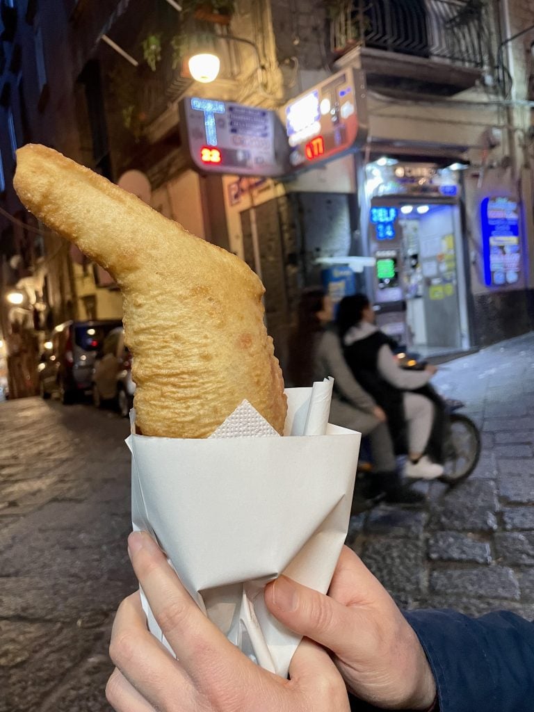 Two hands holding a napkin-wrapped fried calzone-like fried pizza on the streets of Naples.