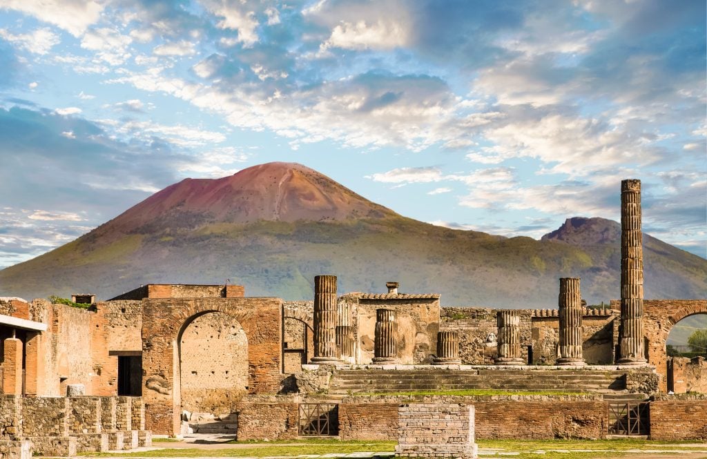 Columns and ruins in the city of Pompeii, the volcano of Vesuvius hovering in the background.