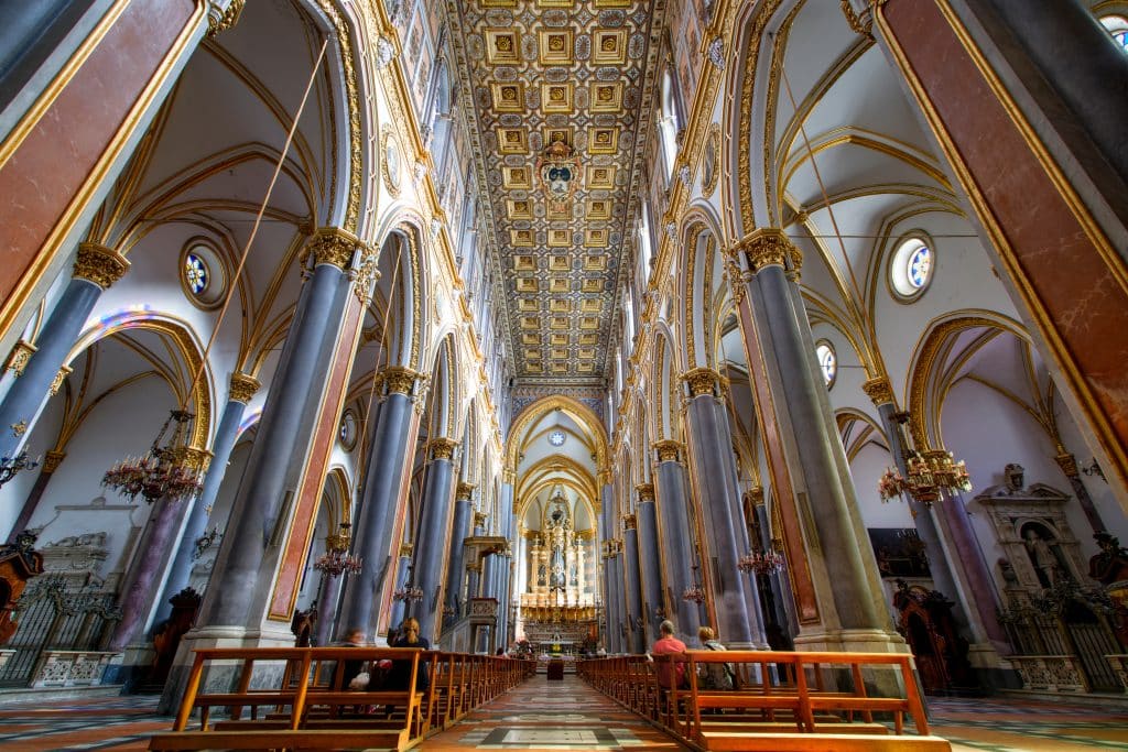 A cathedral in Naples with high ceilings, gothic arches and pillars, covered in panels of red, blue, and gold.