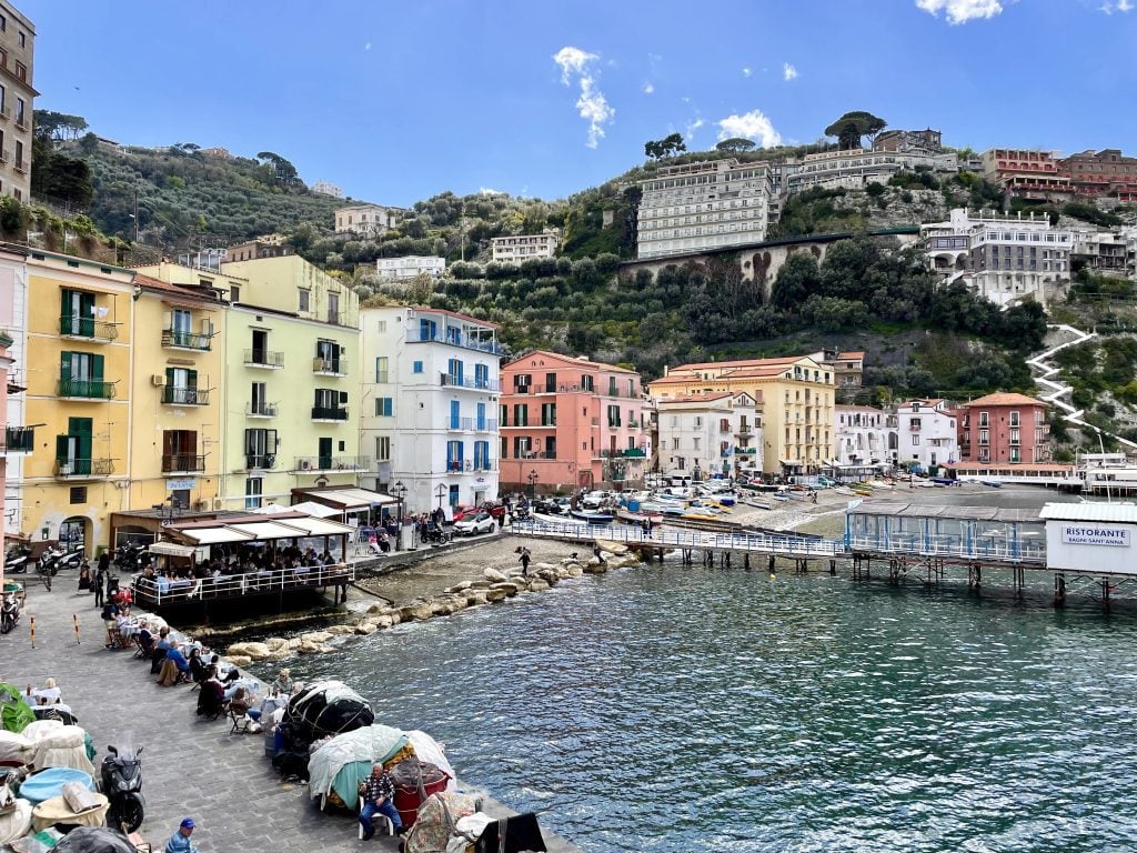 A seaside town with lots of colorful buildings, a small beach, and outdoor restaurant tables overlooking the water.