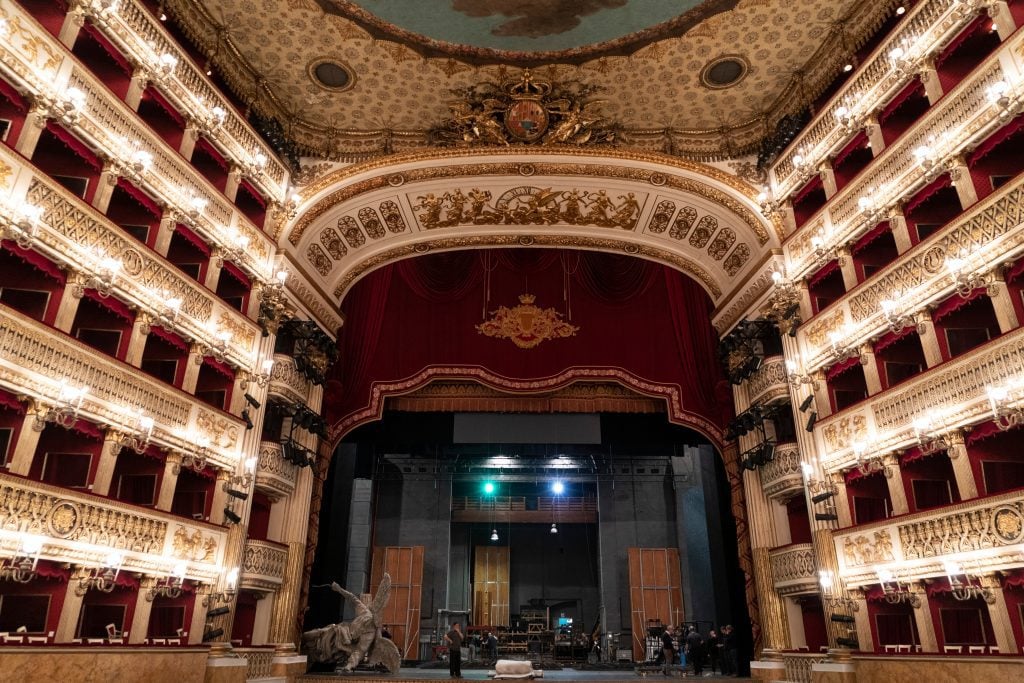 A darkened theater decorated in bright red, with lots of rows of box seats surrounding each side.