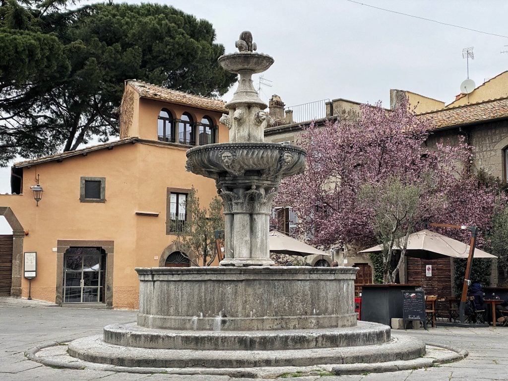 A stone fountain in the center of a small piazza in the city of Viterbo.