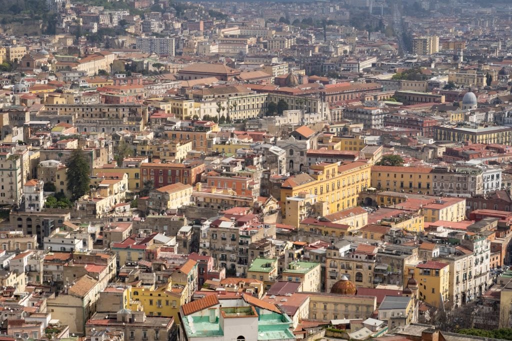 A far-away view of the Naples skyline, with the sun drenching the buildings in light.