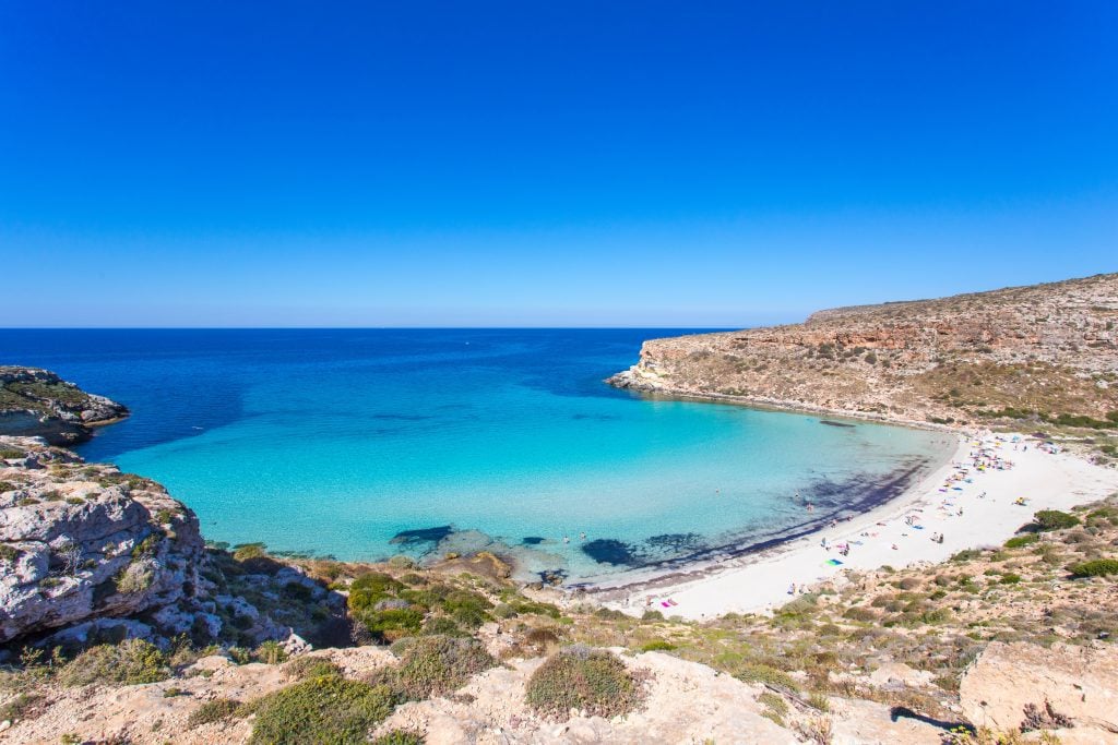 Aerial view of a beach with stunning blue waters and white sand in Lampedusa, one of the best places to visit in Sicily