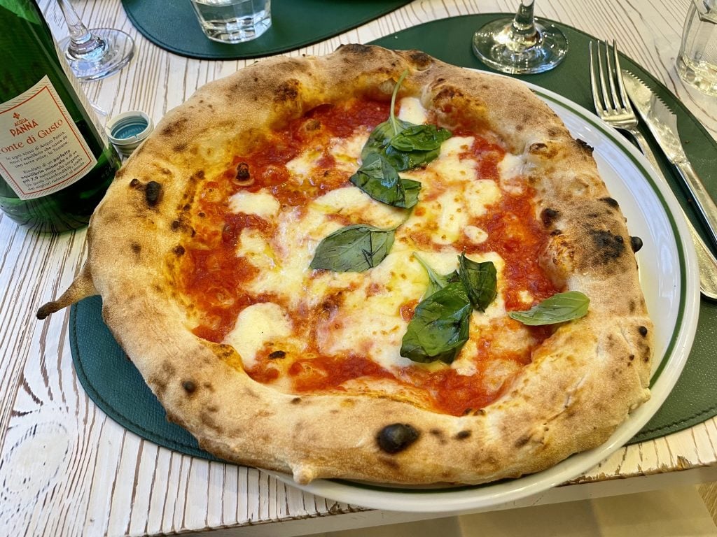 A Neapolitan margherita pizza with a puffy crust, mozzarella, tomato, and lots of basil leaves.