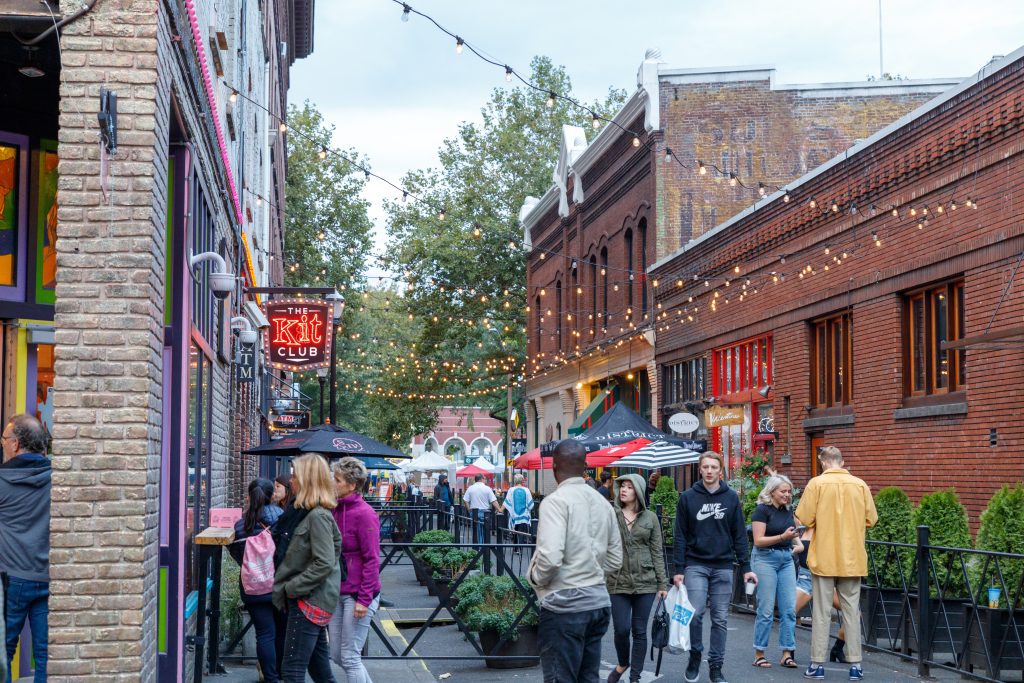 People milling outside a red brick bar with string lights in Portland, Oregon.