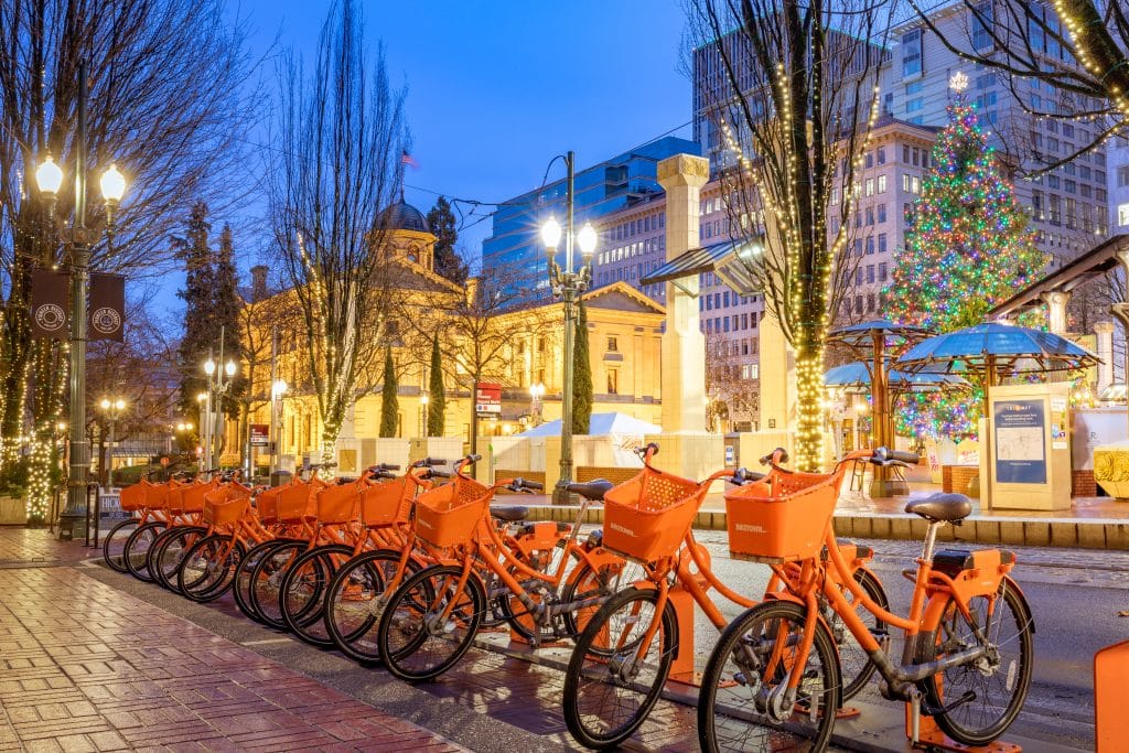 A row of bright orange rental bikes in front of illuminated city buildings at night.