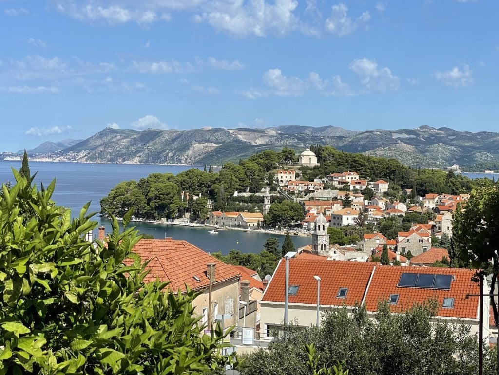 A tiny Croatian town, Cavtat, with lots of white stone orange roofed buildings set on a wooded peninsula surrounded by sea.