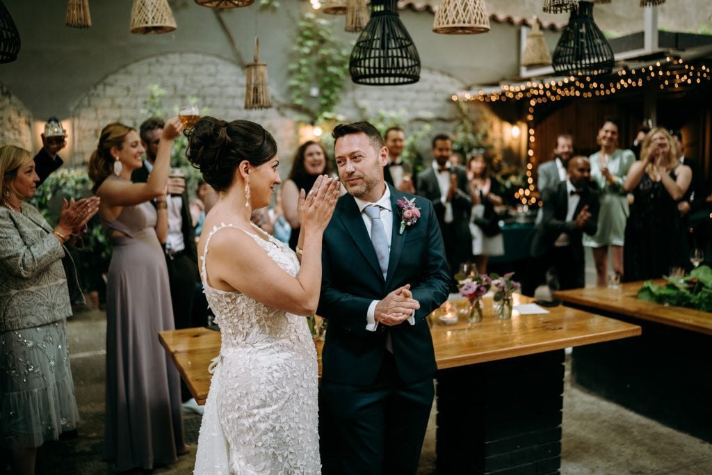 Kate and Charlie at their wedding reception. Kate is clapping and Charlie is looking at Kate with love.