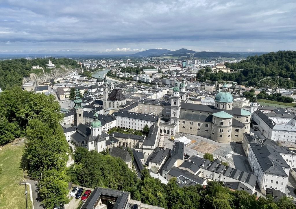 An aerial view of Salzburg, with lots of white and gray Italian-style buildings next to a blue river.