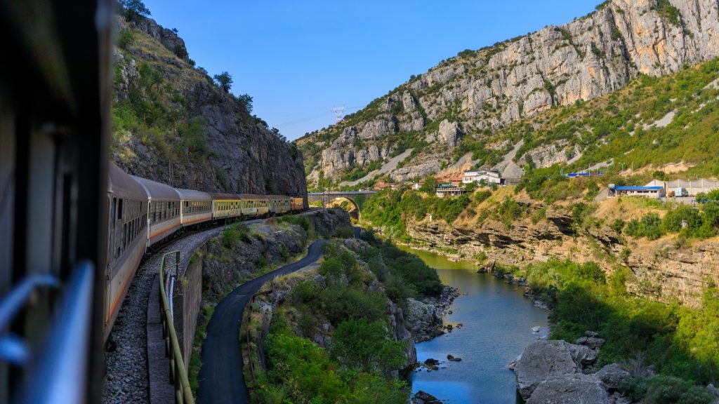 The view of a train curving around tracks in a mountainous green atmosphere.