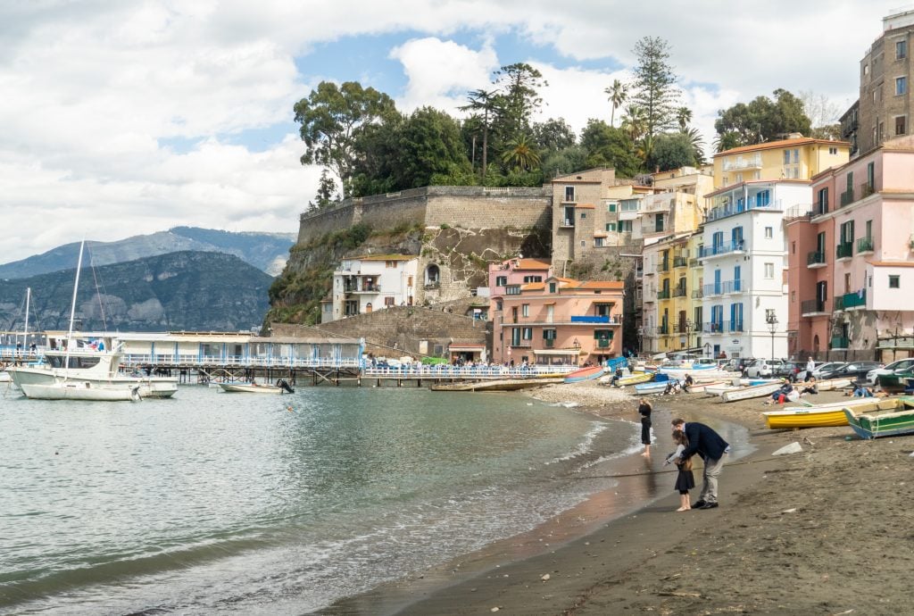 A father and daughter walking on a small beach on a cloudy day in Sorrento.