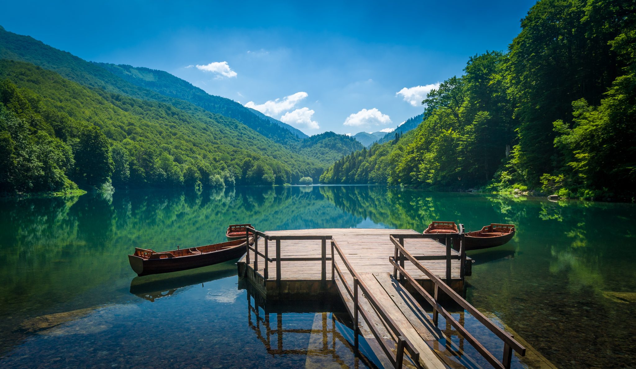 A wooden dock on a calm teal lake surrounded by mountains and forest.