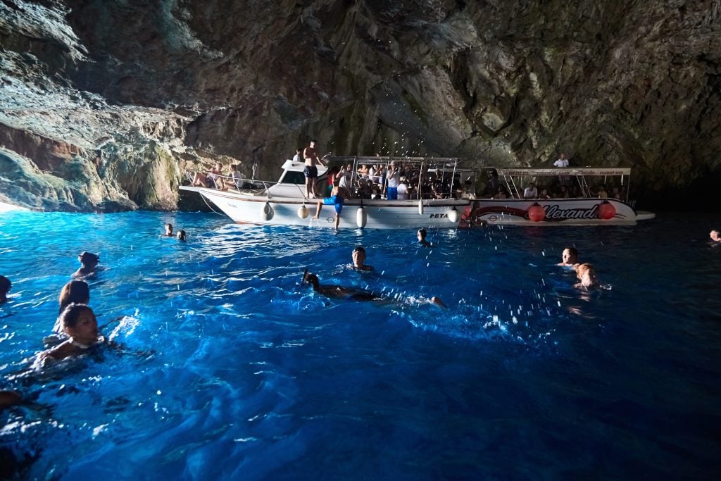 A boat and people swimming in the bright blue water in a cave.