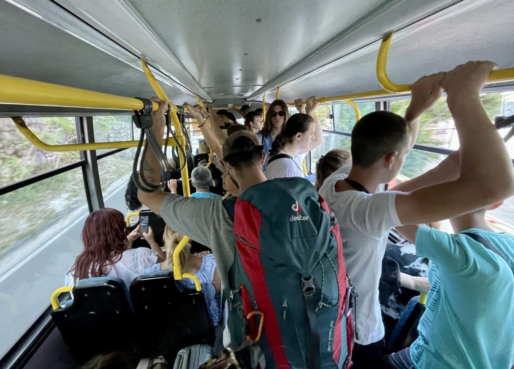 People squished into a public bus, some hanging onto railings.