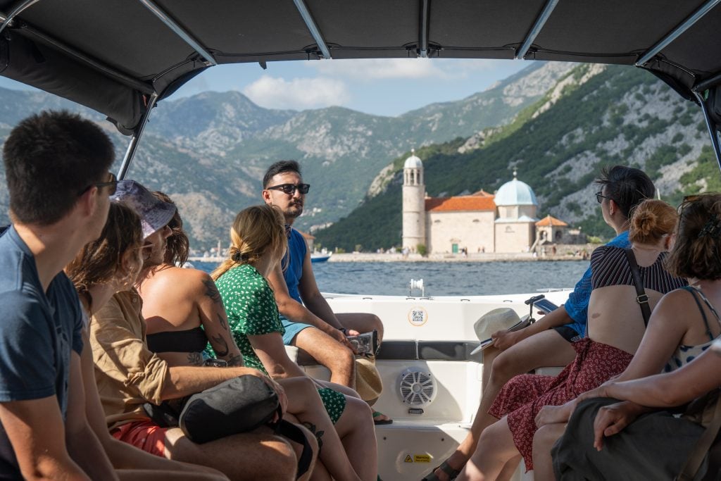 People riding a boat, with the tiny church-topped island in the distance.