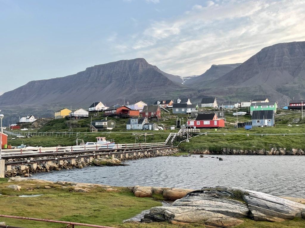 A small Greenlandic town with brightly colored cottages against a steep green mountain.