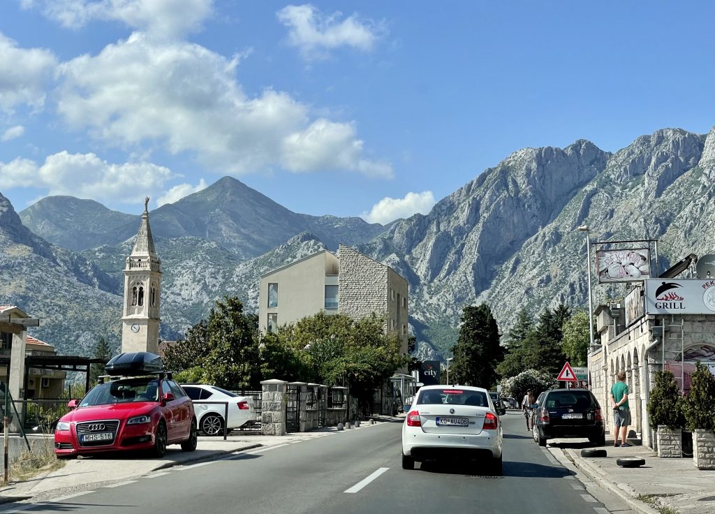 Cars driving down a road in Montenegro, tall mountains rising up in the distance.