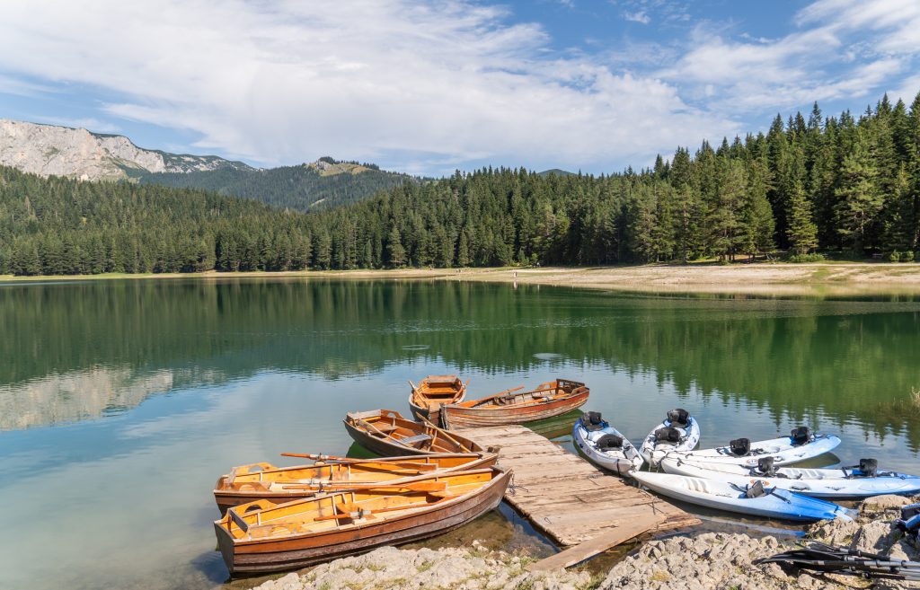 Kayaks and wooden boats perched on the dock on a reflective lake surrounded by forest and mountains.