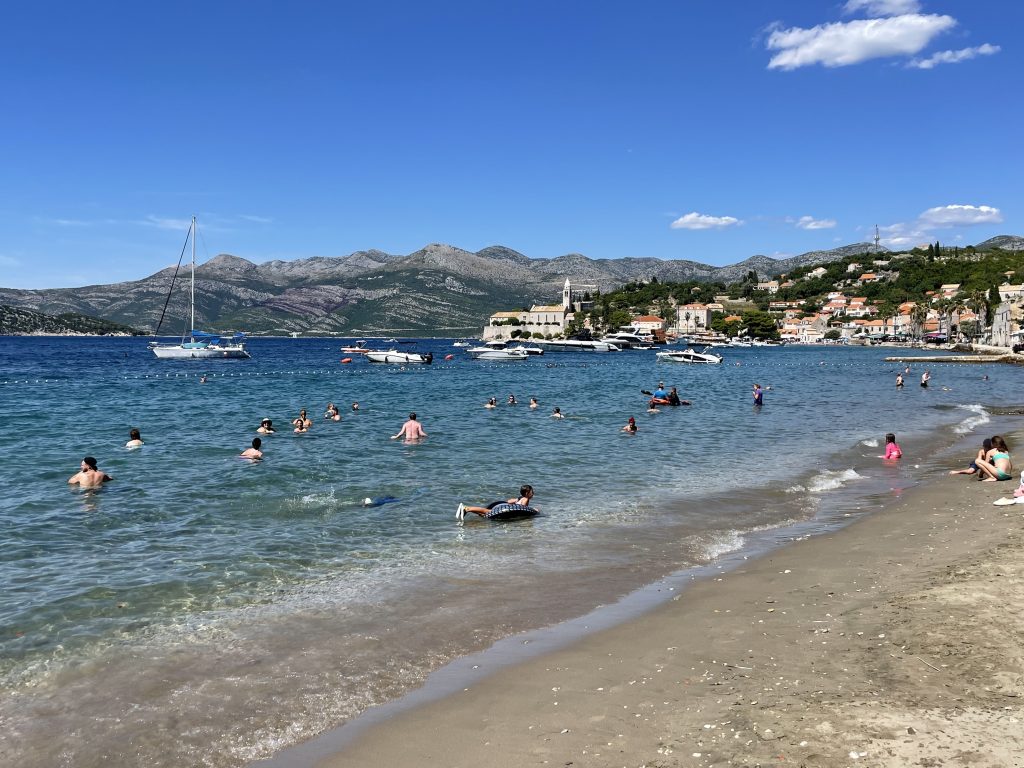 A rare sandy beach in Croatia, lots of kids and adults swimming in the clear turquoise water!