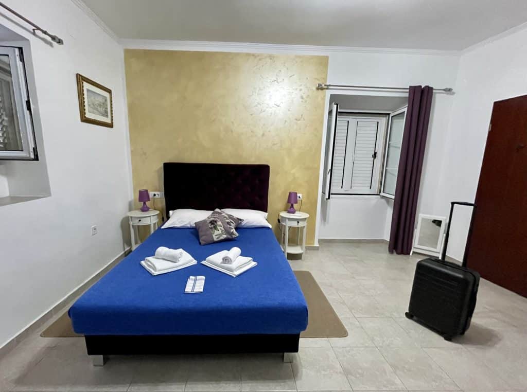 A simple apartment in Montenegro with a queen-sized bed topped with towels, two small end tables, and almost nothing else in the room.
