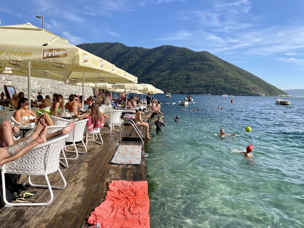 People swimming in the bright blue Bay of Kotor next to a bar built on a cement block.
