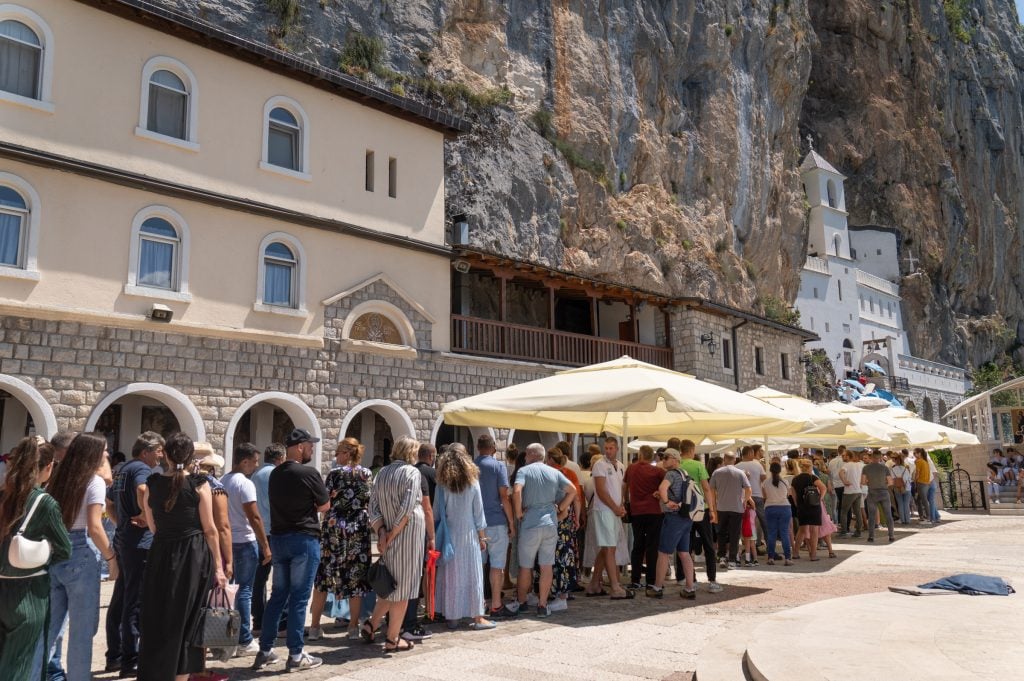 A long line of people waiting to enter a church built into a rocky cliff.