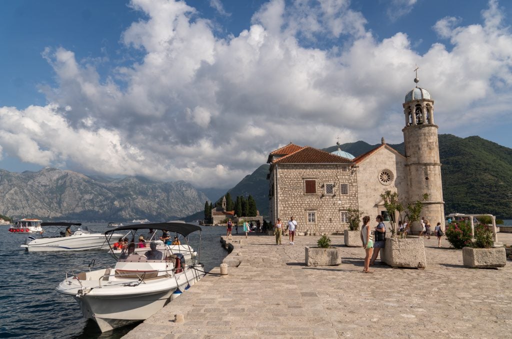 A small concrete island with a chapel built on it, surrounded by boats.