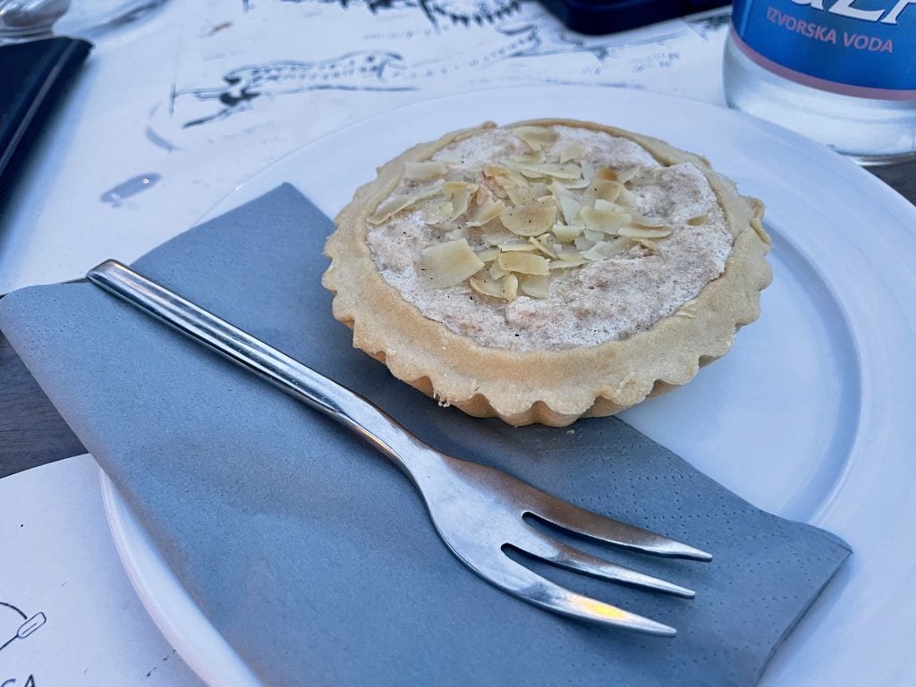 A small round Perast Cake topped with shaved almonds and set on a plate with a fork.