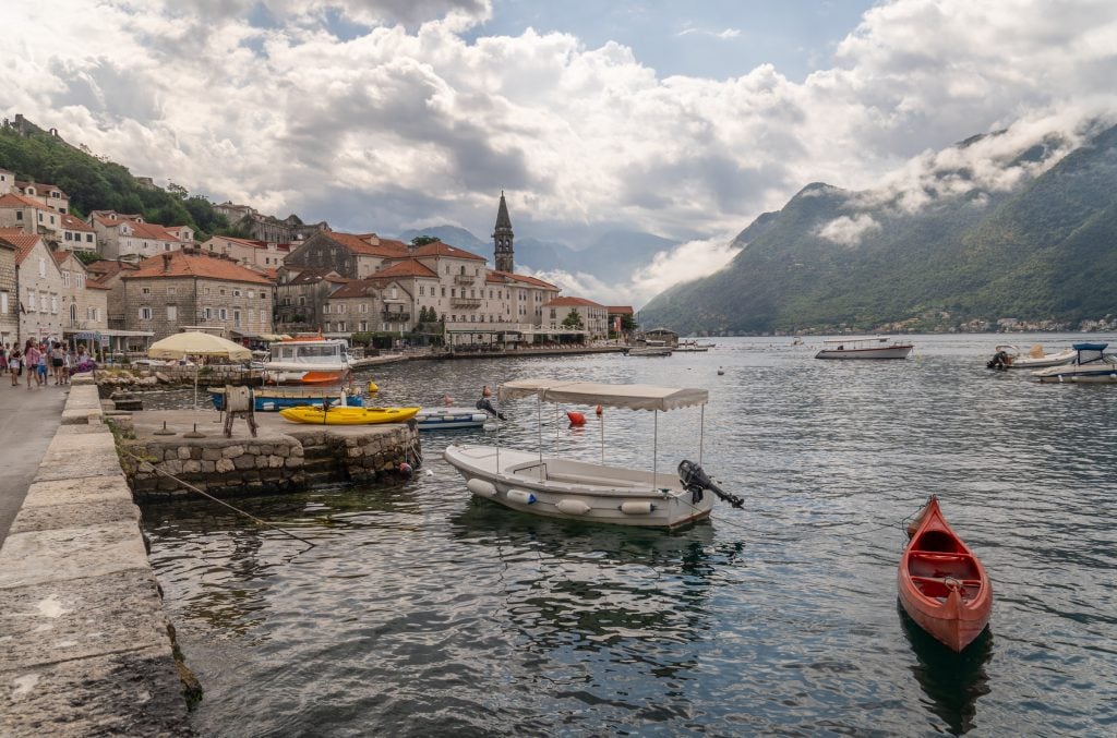 The old town of Perast on a rainy, cloudy day, with overcast skies and boats on the gray water.