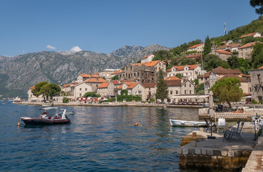 The old town of Perast, with lots of stone buildings, trees squeezed between them, and boats in the water.